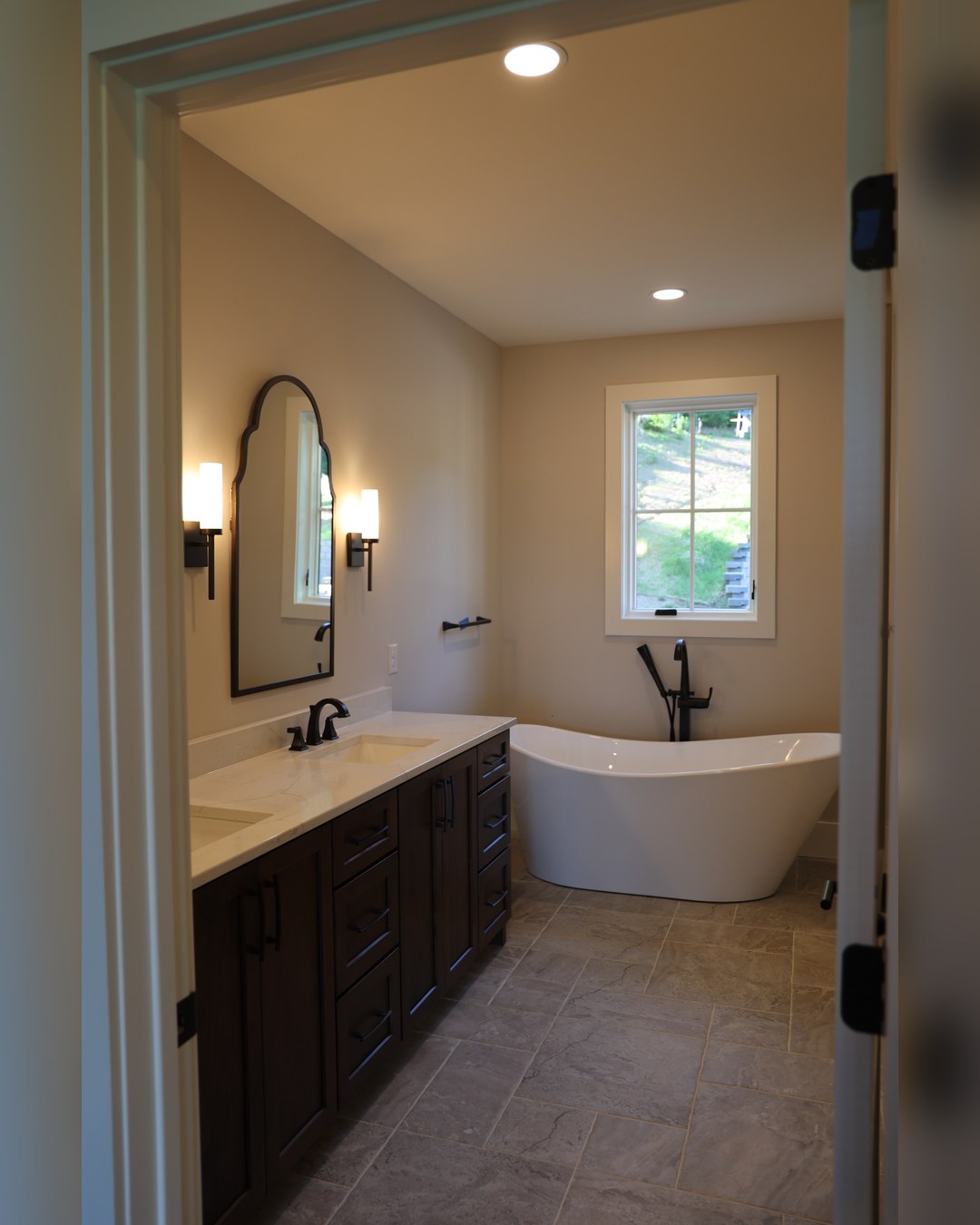 Bathroom with a freestanding tub, black fixtures and a window over the vanity